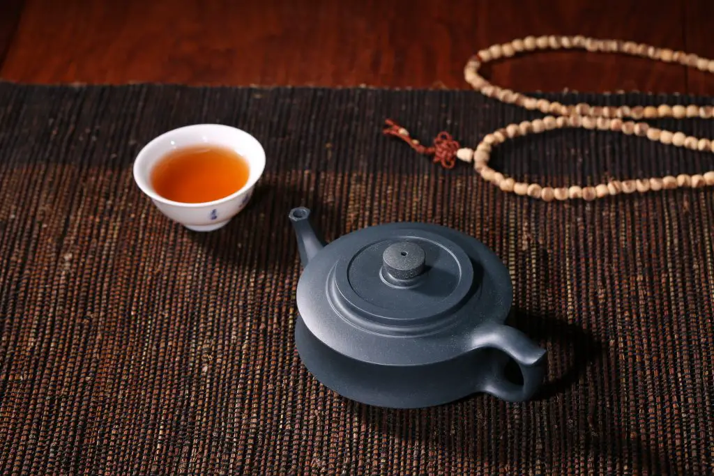 teapot sitting next to a small cup of tea on a rug