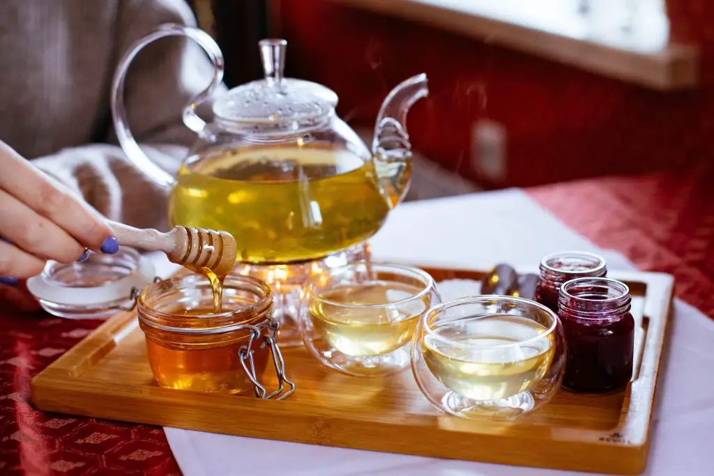 Tea pot with tea placed next to a mason jar of honey