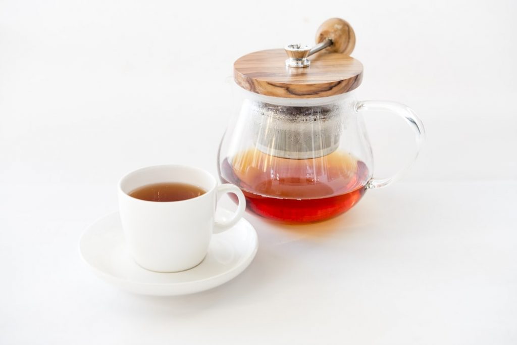 A tea infuser beside a tea-filled cup on a saucer