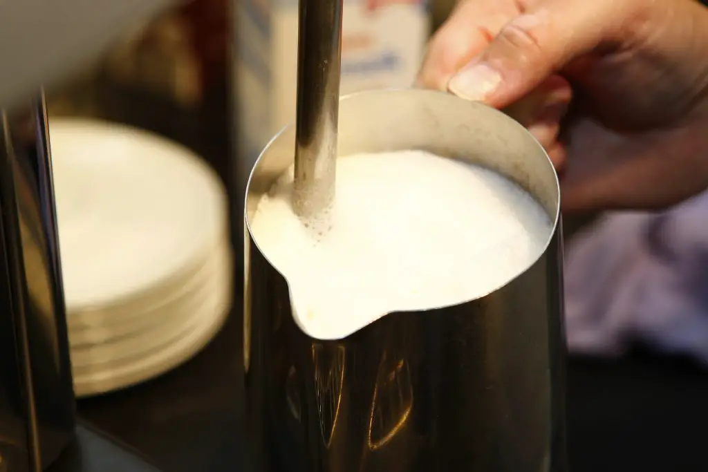 A barista using a milk frother
