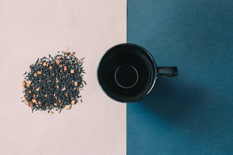 A black mug beside loose tea leaves scattered on a surface