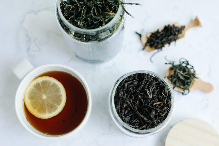 Two jars of loose tea leaves and a cup of tea with sliced lemon on top